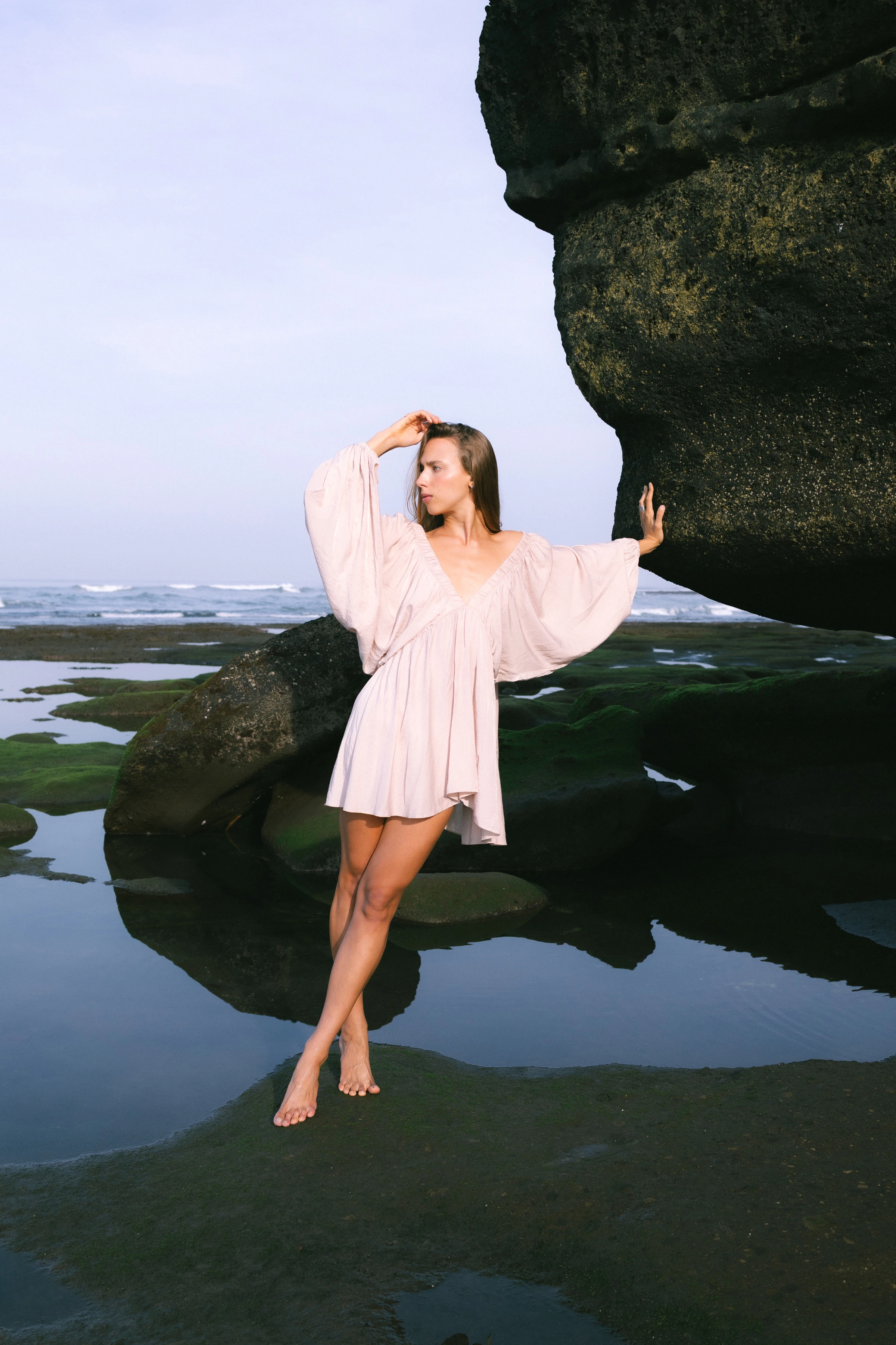 A woman in a pale pink dress beside a coastal rock and tidal pools