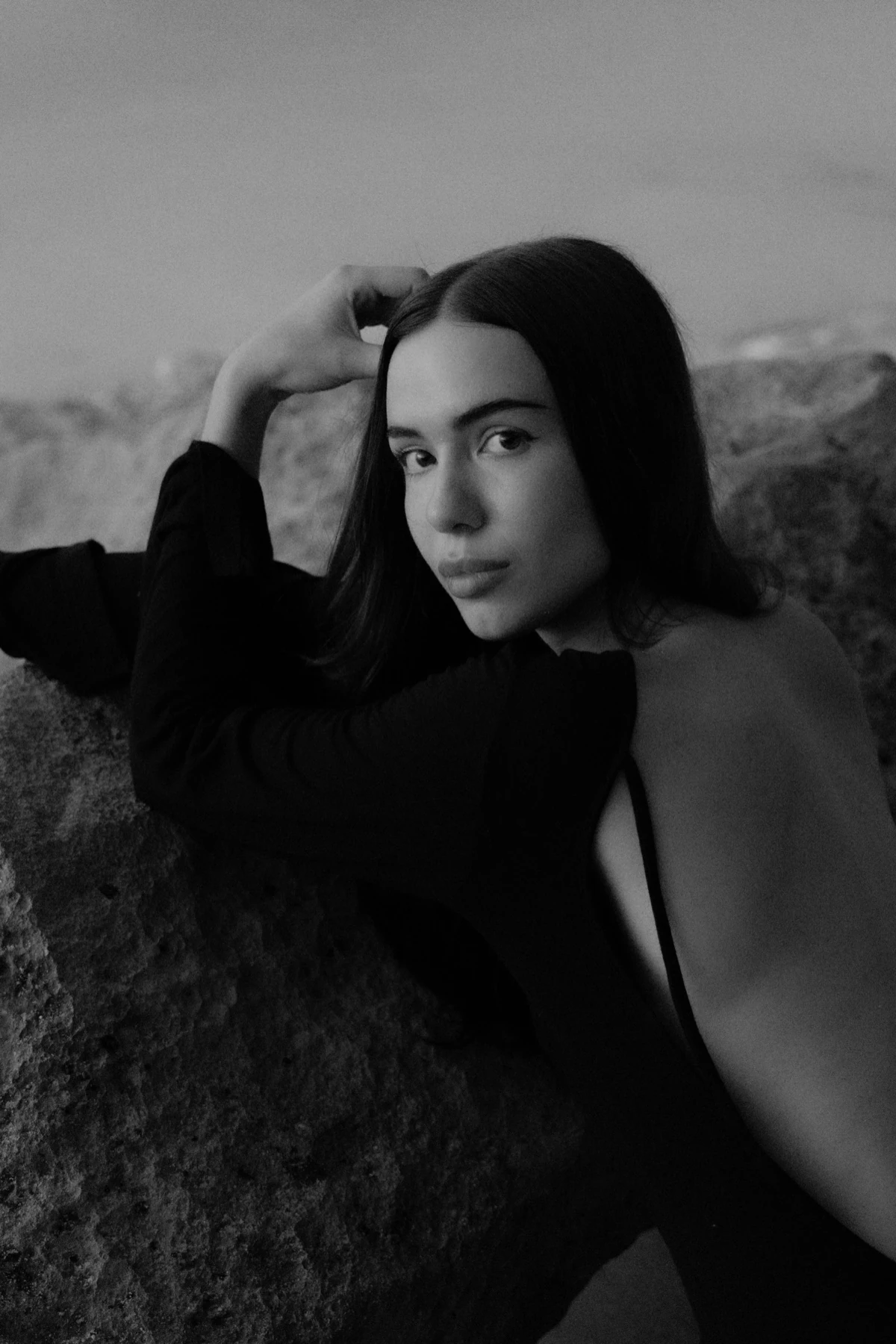 Close black-and-white portrait of a woman reclining against coastal rocks