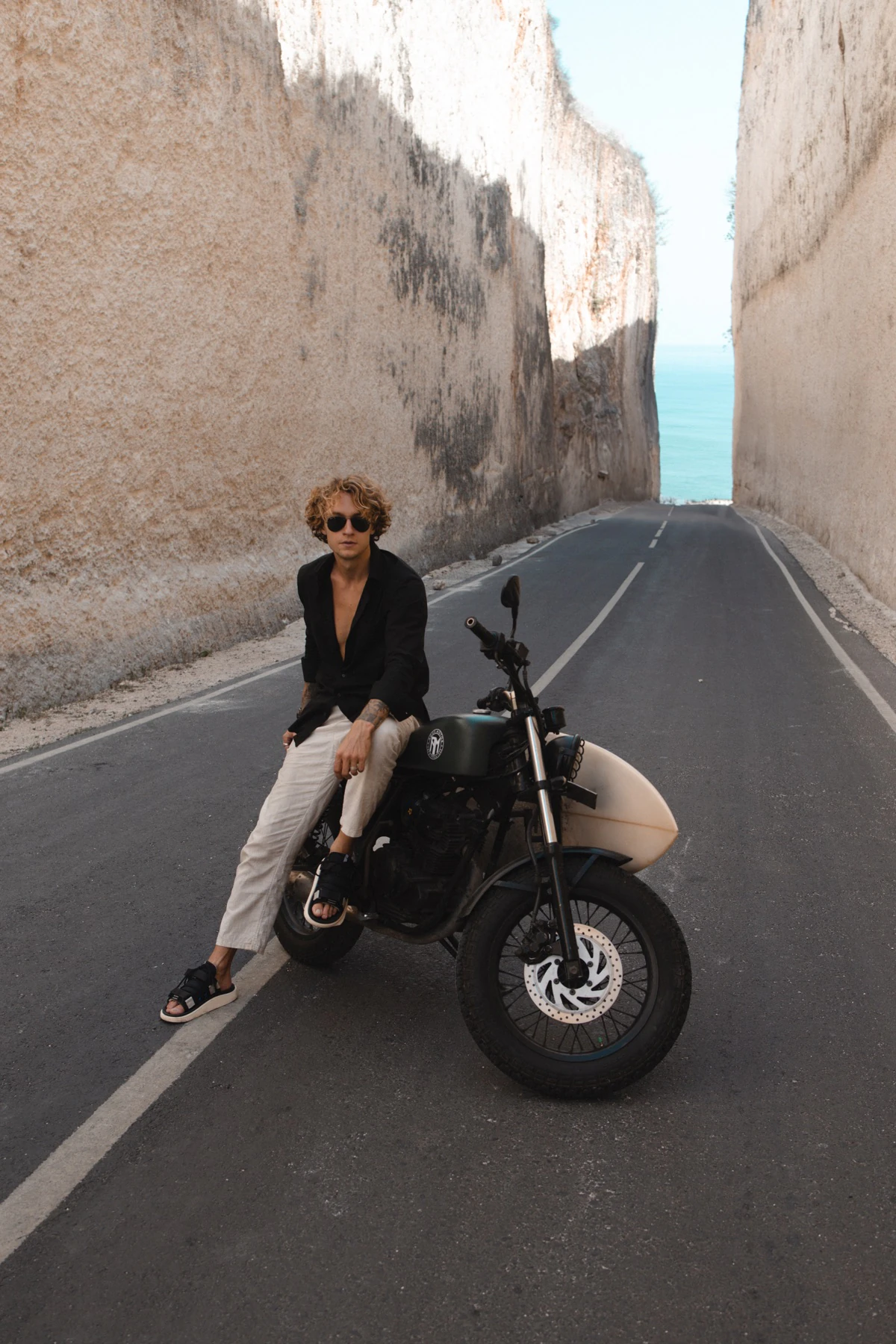 A man seated on a motorcycle between tall stone walls